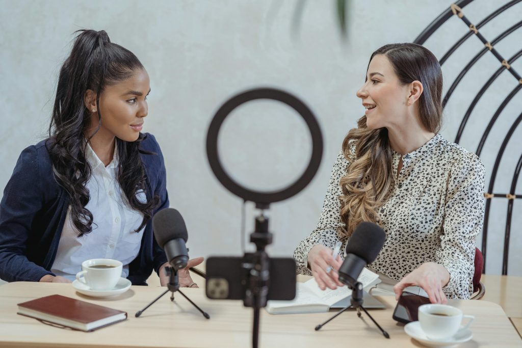 Two girls converse together with podcast and recording equipment in front of them