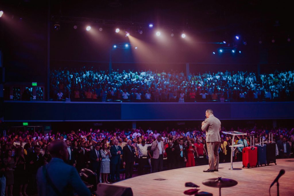 a presenter stands on a stage, in front of a large crowd