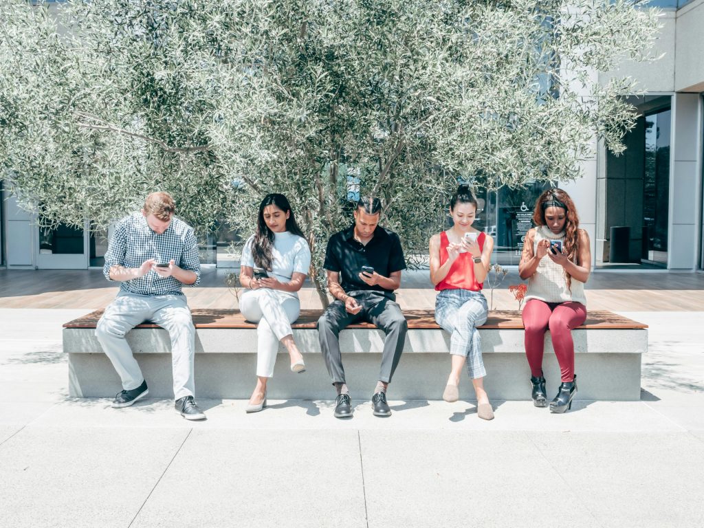 A group of people sit on a bench, but focus on their phones instead of each other